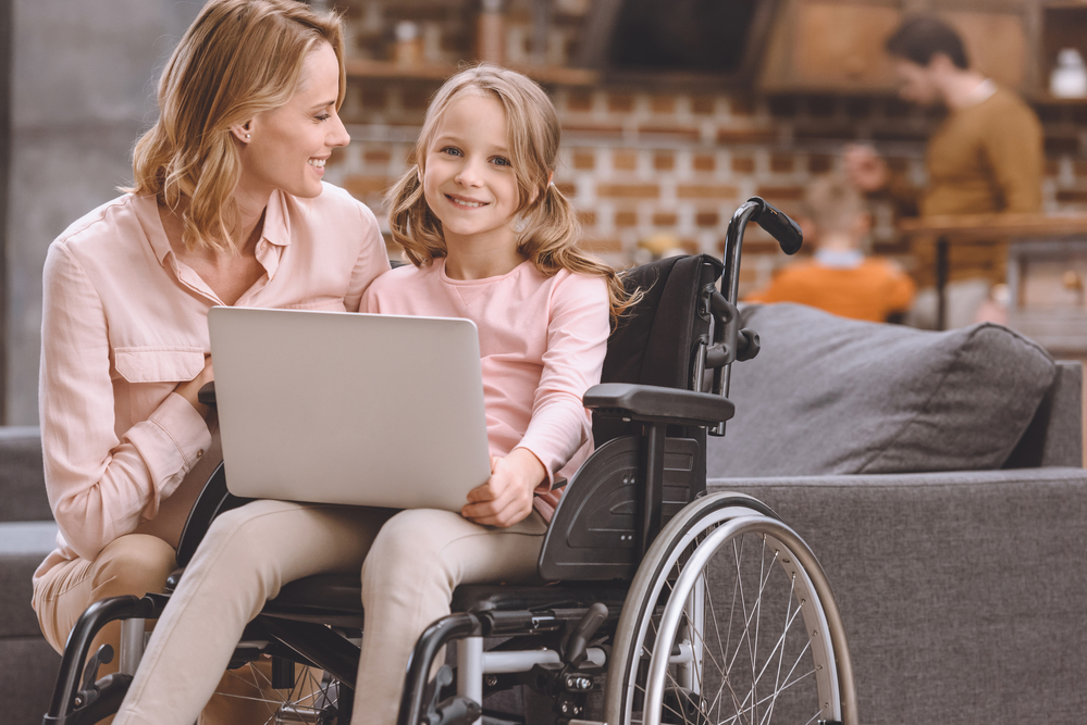 A little girl in a wheelchair with her mom next to her on the couch